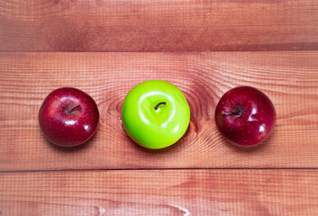 Two red and one green apples on a wooden background: the difference between apple varieties, the benefits and harms of different apple colors, space for text 