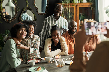 Happy African family smiling at camera on mobile phone while sitting at dining table at home