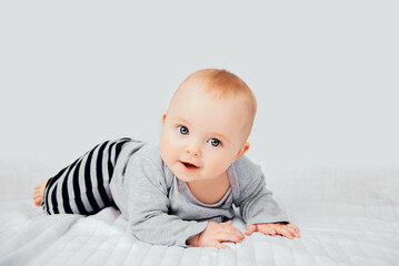 Seven month old baby child sitting on bed. Cute smiling little infant girl on white soft blanket. Charming blue eyed baby. Copy space.