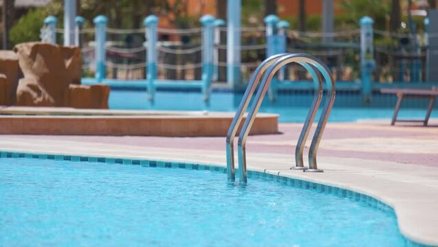 Close up of swimming pool stainless steel handrail descending into tortoise clear pool water. Accessibility of recreational activities concept