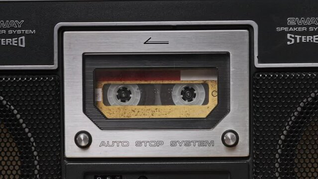 Vintage yellow audio cassette tape rotates in deck of old tape recorder. Audiocassette with blank label in retro player spinning and playing. Close-up. Call recording, retro playback, reel with tape