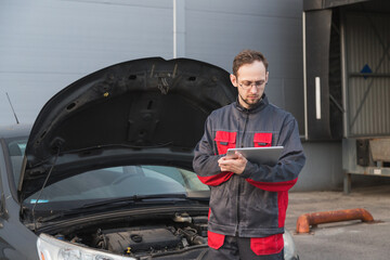 Caucasian mechanic in uniform using tablet pc at car repair station. Car maintenance