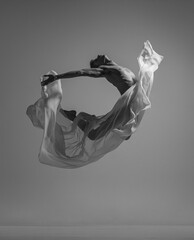 Flight. Black and white portrait of graceful muscled male ballet dancer dancing with fabric, cloth isolated on grey studio background. Grace, art, beauty concept. Weightless, flexible.