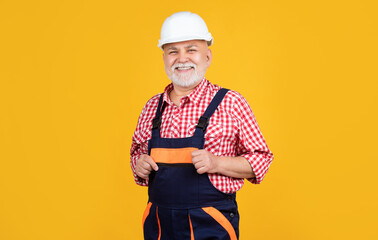 happy old man builder in helmet on yellow background