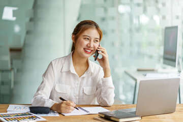 Beautiful young Asian business woman charming smiling and talking on the mobile phone in the office.