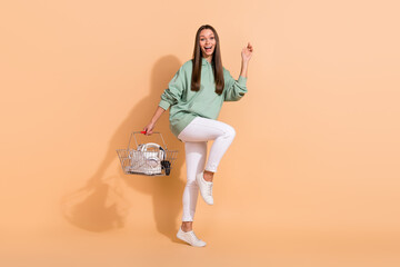 Full length body size view of attractive cheerful girl holding devices goods dancing isolated over beige pastel color background