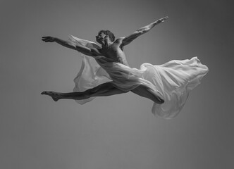 Desire. Black and white portrait of graceful muscled male ballet dancer dancing with fabric, cloth isolated on grey studio background. Grace, art, beauty concept.