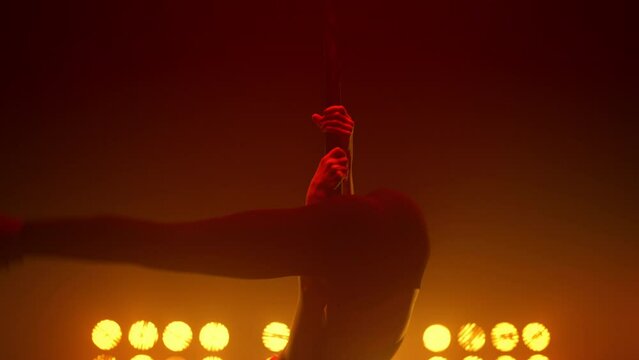 Girl dancer performing acrobatic elements pole dance in nightclub stage closeup.