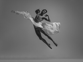 Black and white portrait of graceful muscled male ballet dancer dancing with fabric, cloth isolated...