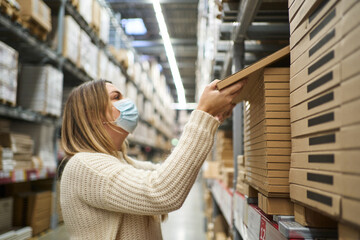 a woman in a protective mask takes boxes in a self-service warehouse in a furniture store. packaging in a self-service warehouse furniture in boxes, rows in a warehouse