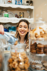 Beautiful young female seller working in a confectionery shop or bakery. She is selling and packing delicious sweets.