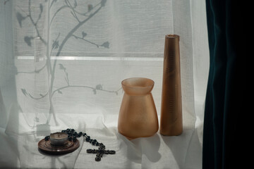 A cross, a candle create a composition at the window. Symbols of Christianity in the interior of the house.