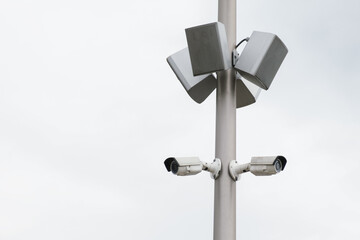 Two small white CCTV cameras and loudspeaker speakers on a pole . Security, video surveillance,...