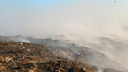 Burning pile of garbage at dump ground or landfill releasing toxic smoke in environment and...