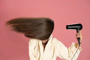 Woman drying her long hair with electric fan on a pink background