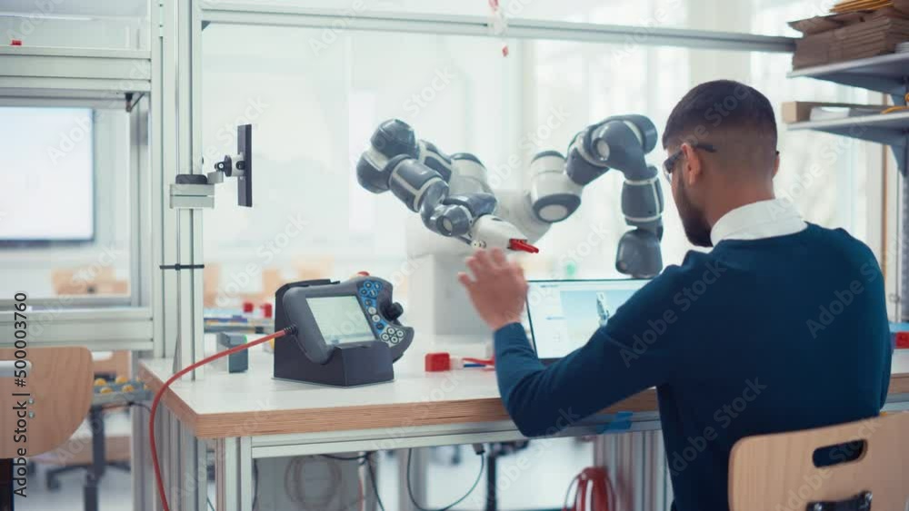 Poster Male Industrial Robotics Engineer Uses Laptop Computer to Program and Manipulate Robot Arm for Lifting, Moving Objects. Black Man Touching Controller and Writing Code. Machine Learning Concept