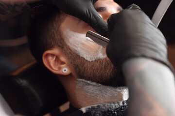 Professional hairdresser working with bearded client in barbershop, closeup