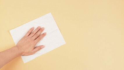 Obraz premium Hand is wiping and hold white paper tissue on cream ivory color background. Closeup. Empty place for text .Top down view.
