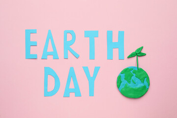 Phrase Earth Day and planet model with green seedling on pink background, flat lay