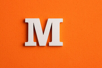 Alphabet letter M - White wood piece on orange foamy background