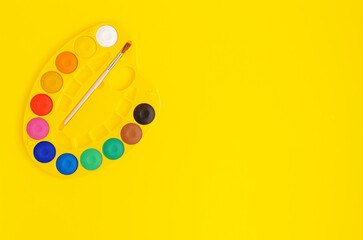 Palette of watercolor paints on yellow background. Copy space, top view.