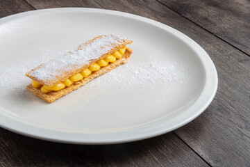 Puff pastry pantxineta with lemon cream and icing sugar on a white plate on a rustic wooden background. Typical dessert from the Spanish Basque Country.
