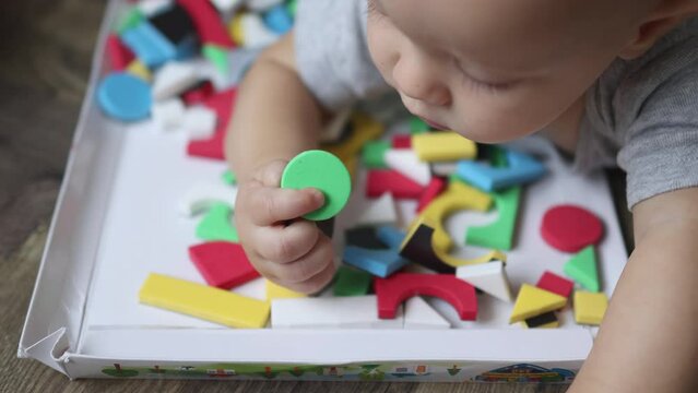 baby infant lying on floor, exploring colorful pieces toys, tasting, putting in mouth, trying to bite them. childhood, learning, developing feelings, leisure activities concept. high angle view