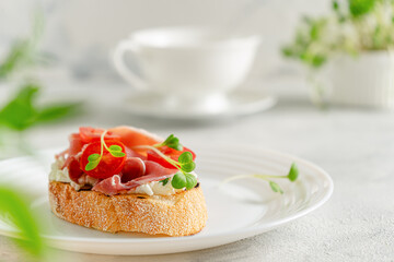 Obraz na płótnie Canvas Ciabatta toast with prosciutto or jamon, tomato and soft cheese. Mediterranean breakfast. Copy space