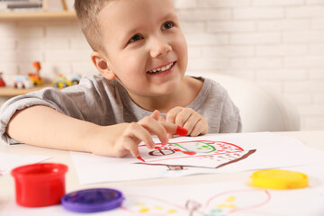 Little boy painting with finger at white table indoors