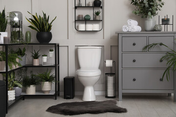 Fototapeta na wymiar Stylish bathroom interior with toilet bowl and many beautiful houseplants