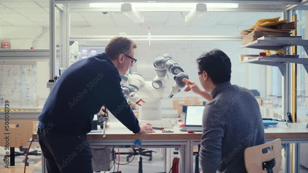 Aufkleber Adult Engineer Changes Position of Robot Arm with Controller while Young Specialist Discuss with him and Hold Processor. Startup and Innovative Technologies in Robotics Concept