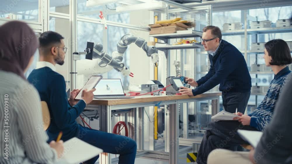 Poster Chief Male Engineer Manipulate with Robot Arm and Talk with Young Computer Specialists at Factory Meeting Room, They Find Problem Solutions. Developing and Robotics Concept
