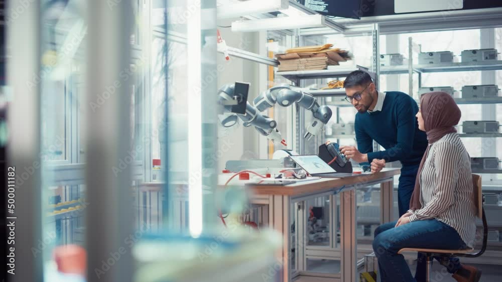 Aufkleber Black Male Engineer Raise Robot Arm with Controller while Female Developer in Hijab Write Code at Laptop. People Create Innovative Program. High Tech and Robotics Concept