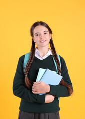 Obraz premium Teenage girl in school uniform with books and backpack on yellow background