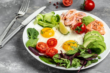 Ketogenic breakfast. Keto low carb salmon, boiled shrimps, prawns, fried eggs, fresh salad, tomatoes, cucumbers and avocado. top view. Low carb diet concept. high fat diet