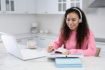 African American woman with modern laptop and headphones studying in kitchen. Distance learning