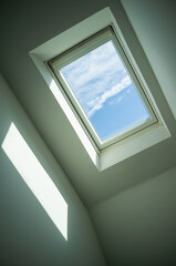 Closed roof window through which you can see the blue sky and white clouds on a sunny day. Bottom view.