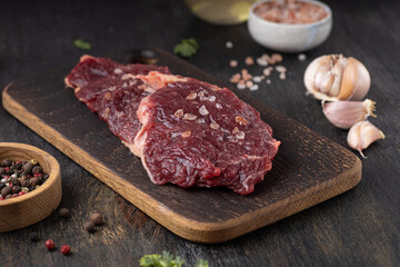 Raw fresh meat Ribeye Steak, seasoning and fresh tomato on wooden background