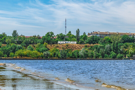 View of the coastline of Mykolaiv from Strilka beach on the Inhul River, Ukraine. A large sculpture with the name of the city among the greenery against the background of water