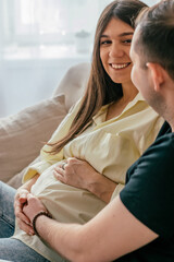 The husband hugs his pregnant wife, sitting at home on the couch..Family and pregnancy concept.Selective focus,close up.