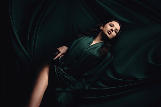 fashionable photo of a beautiful woman with brunette hair in a dark green dress. Dress made of fabric fluttering creating a background