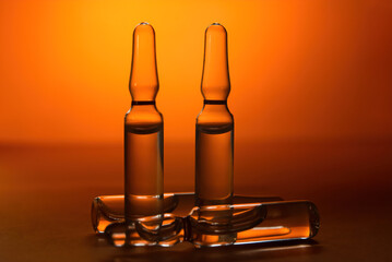 Two transparent sealed ampoules on an orange background stand upright, and two ampoules lie behind...