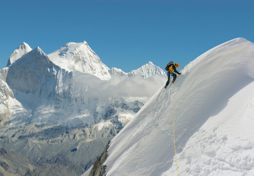 Mountain climber climbing steep snowed slope in spectacular mountain landscape 
