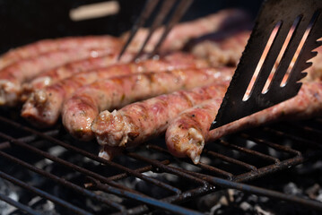 Sausages, traditional Italian 'salsiccia', being turned by a metal shovel, grill on a rustic grill over hot charcoal