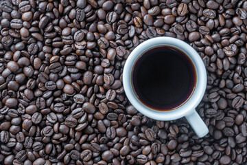 Fototapeta premium White cup of hot black coffee with a background of fresh roasted coffee beans, top view