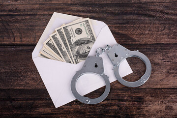 handcuffs lying on an open white envelope with dollars, close-up on a dark background
