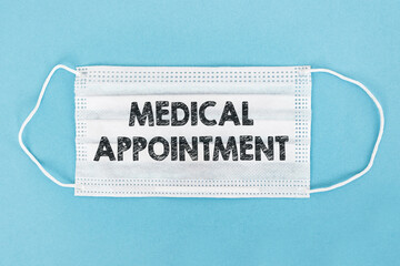 A white medical face mask with text MEDICAL APPOINTMENT on blue background. Medical concept,