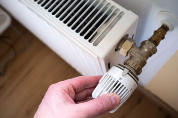 Hand turns the radiator thermostat to the minimum, due to rising gas prices. Concept of energy crisis and economy. 