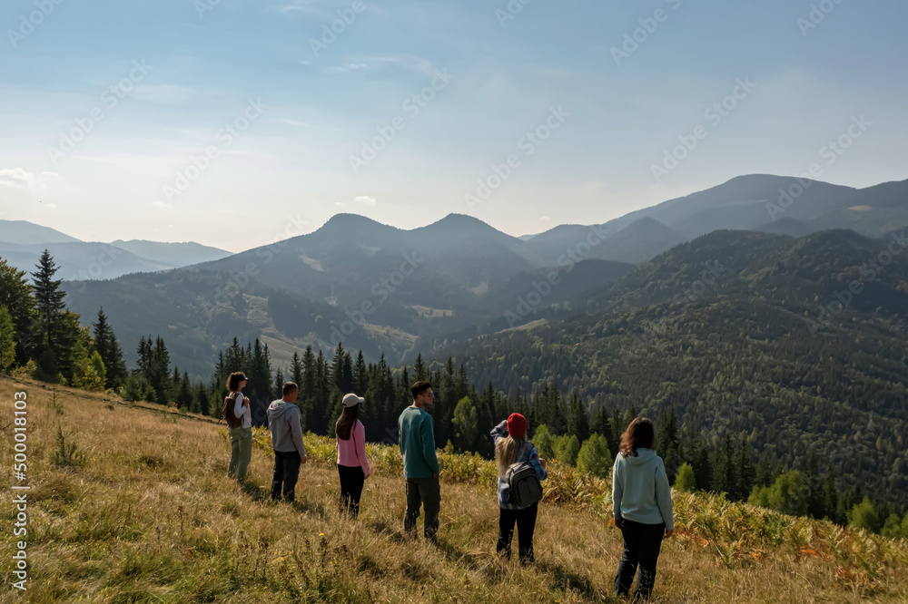 Wall mural group of tourists on hill in mountains, back view