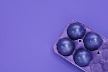 Top view of four violet colored eggs in purple egg paper box on violet background. Painted Easter eggs in shiny very peri trendy color of 2022 year. Happy Easter concept. Shopping, supermarket, food.